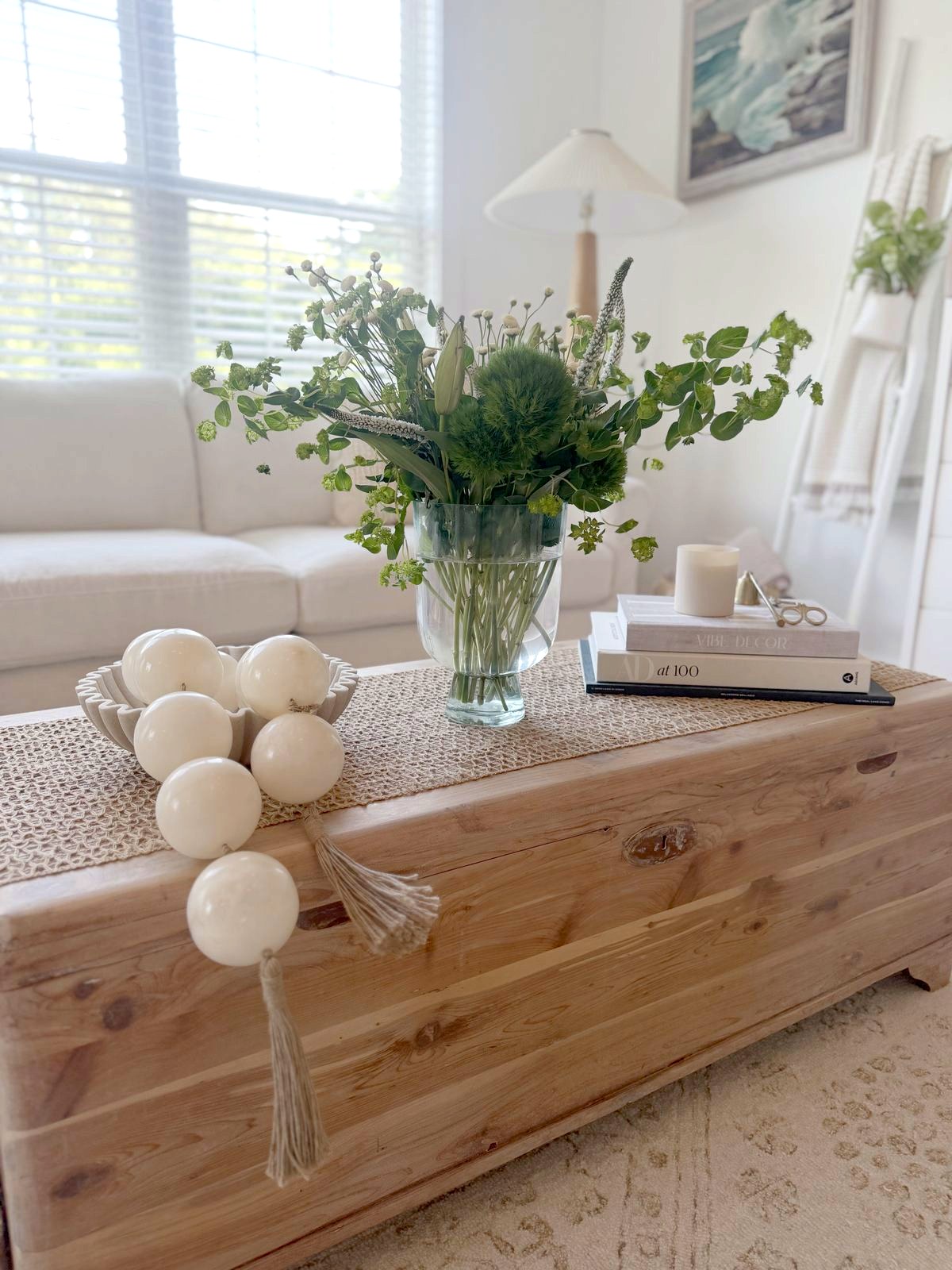 Styled wood coffee table with a green floral arrangement, candle and design books
